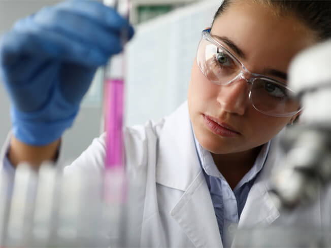 Female scientist in laboratory holds test tube with purple liquid in her hand.