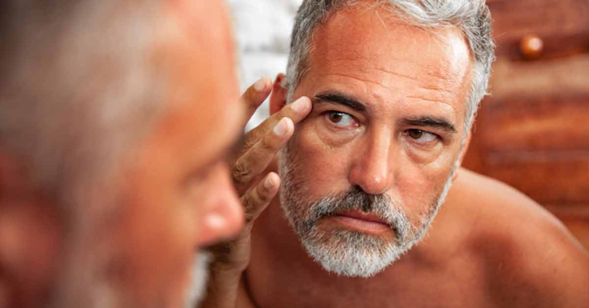 mature man looking in mirror at skin