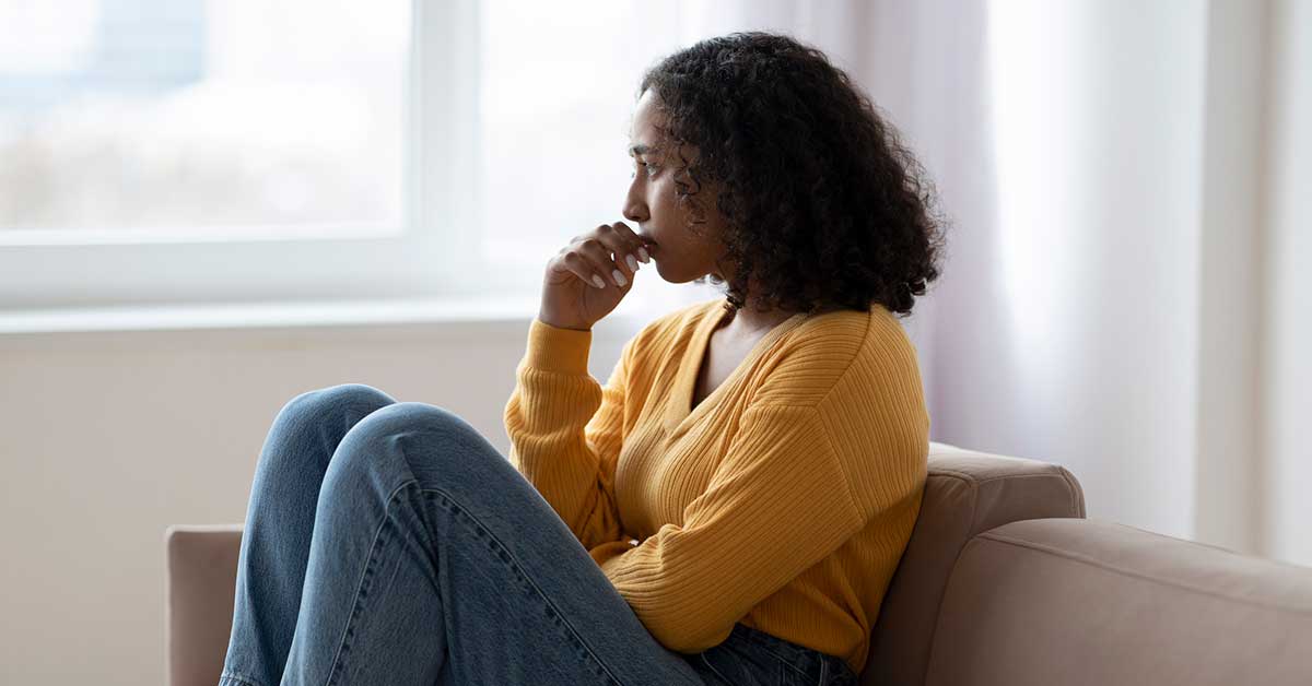 Depressed young black woman suffering from emotional burnout on couch at home