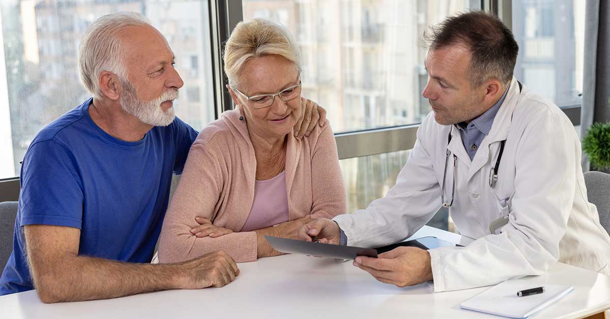 Healthy smiling senior couple feeling cheerful about good news at medical consultation.